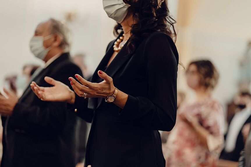 Eine Frau mit Maske hält die Hände zum Gebet erhoben 